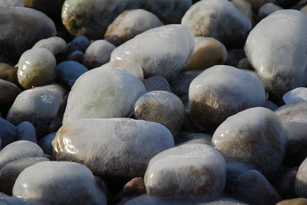 磨砂石质哑铃户外霜近距离关闭海岸覆盖的冰块卵石背景