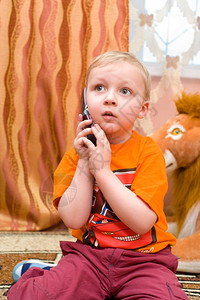 耍狮子小男孩金发的欧洲小男孩通过手机说话波德希瓦洛夫地毯讲话背景