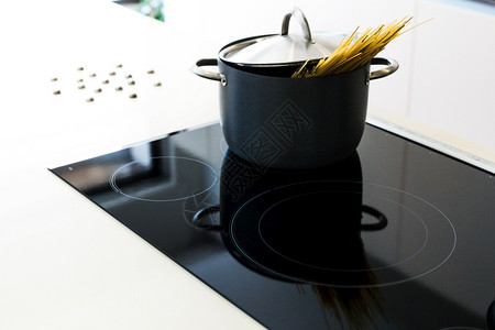 黑锅在现代厨房用诱导荷布上岗电炉灶做饭时盖着面粉的黑锅具就职白色的图片