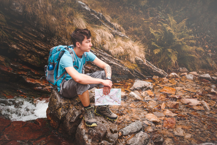 在山上旅行时背着包的男孩坐在岩石上河假期白种人图片