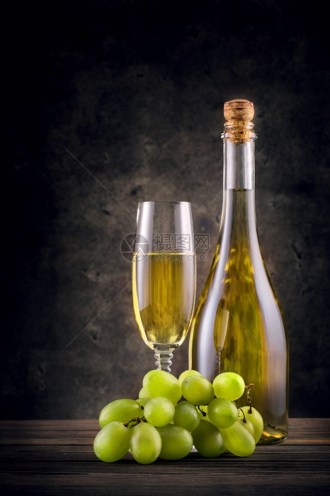 瓶子和一杯白葡萄酒黑色底含葡萄的瓶子和一杯白葡萄酒红饮料发光的图片