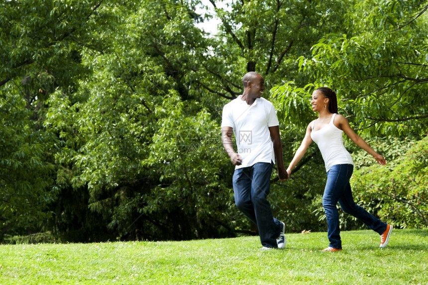 非洲人牛仔布绿色欢笑快乐的美丽笑着微的非裔美国年轻夫妇在公园里玩耍穿着白衬衫和蓝牛仔裤图片