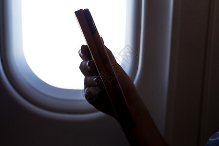 飞机上看书在去度假的途中飞机上阅读平板电脑成人在职的喷射背景