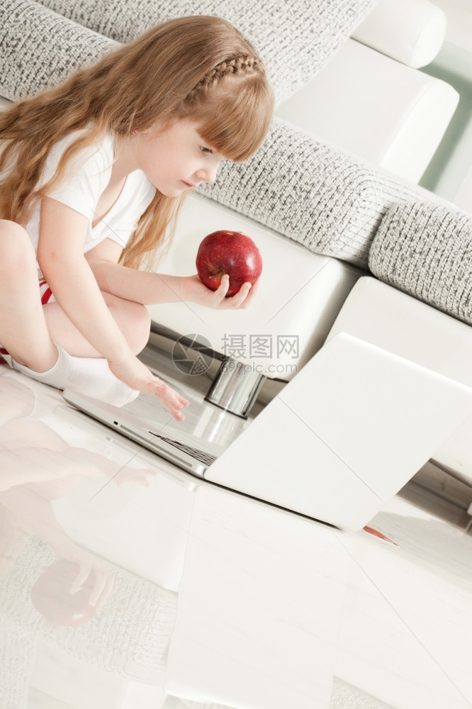 女随意的孩子小女玩笔记本电脑和吃苹果图片