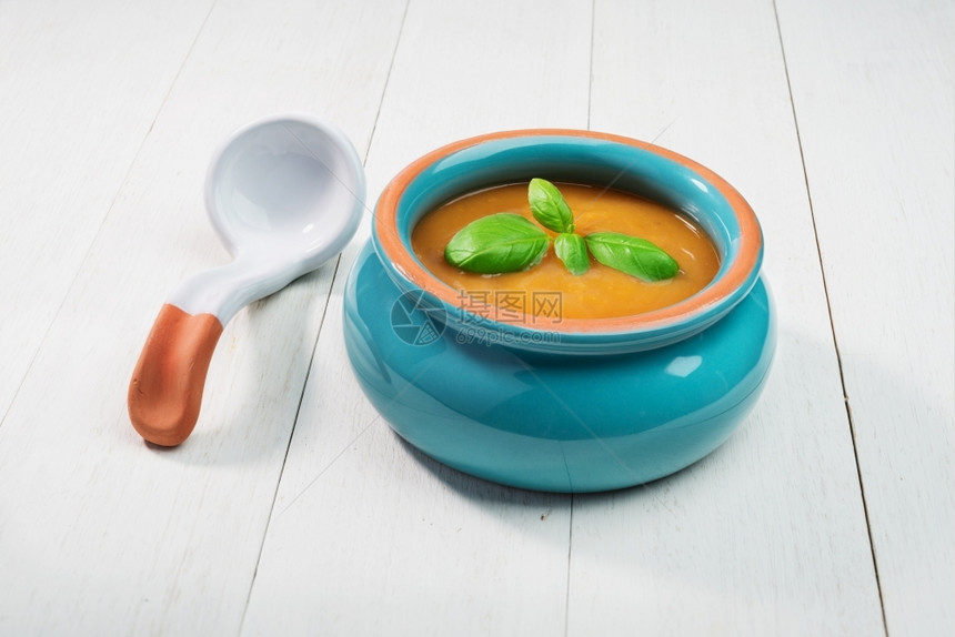 健康热的在陶瓷碗中新鲜的南瓜汤勺子放在旧木制背景上的图片