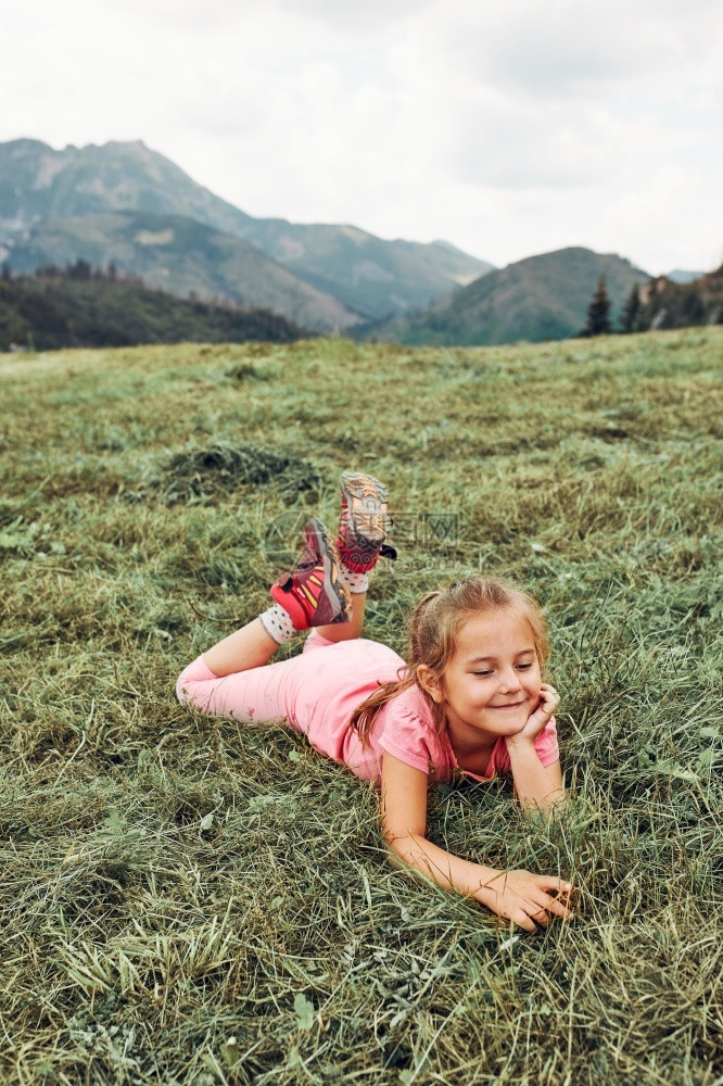 请享用小女孩躺在草地上玩耍享受暑假的夏日期快乐的孩子在田野里玩耍山坡风景的度假旅行中玩女孩在度假期间草地上玩绿色俏皮图片