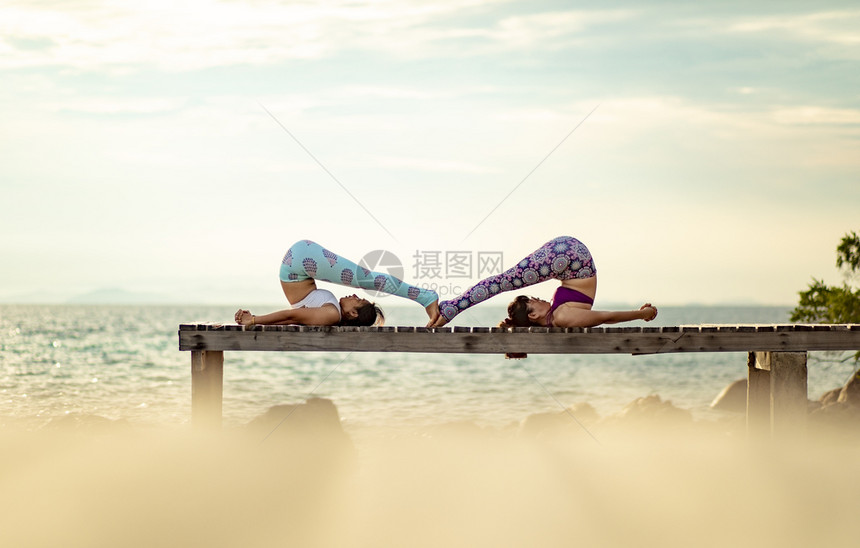 闲暇健康在海滩码头做瑜伽姿势阳光照耀的女子情侣活动图片