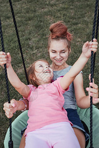 户外少女在后院的一家庭操场上与妹玩耍快乐笑的姐妹们在夏日一起秋千玩得开心真人情一种粘合背景图片