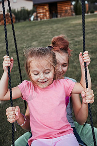 拥抱少女在后院的一家庭操场上与妹玩耍快乐笑的姐妹们在夏日一起秋千玩得开心真人情姐孩子背景图片