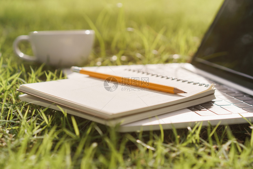 公园笔记本和铅放在记本电脑上而笔记本电脑和咖啡杯放在绿草上户外色图片