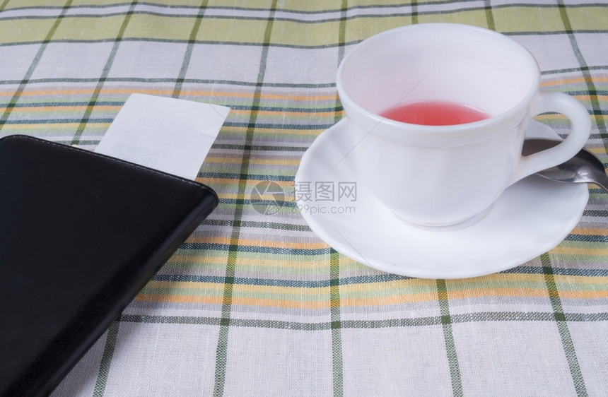完成的常设现金站在桌上的白茶杯和一个黑色文件夹上面有付款收据一杯茶和个黑色文件夹上面有付款单图片