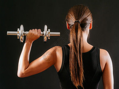照片中一位年轻女背面拍着黑景的低音喇叭在肩上按压训练黑暗的运动员图片