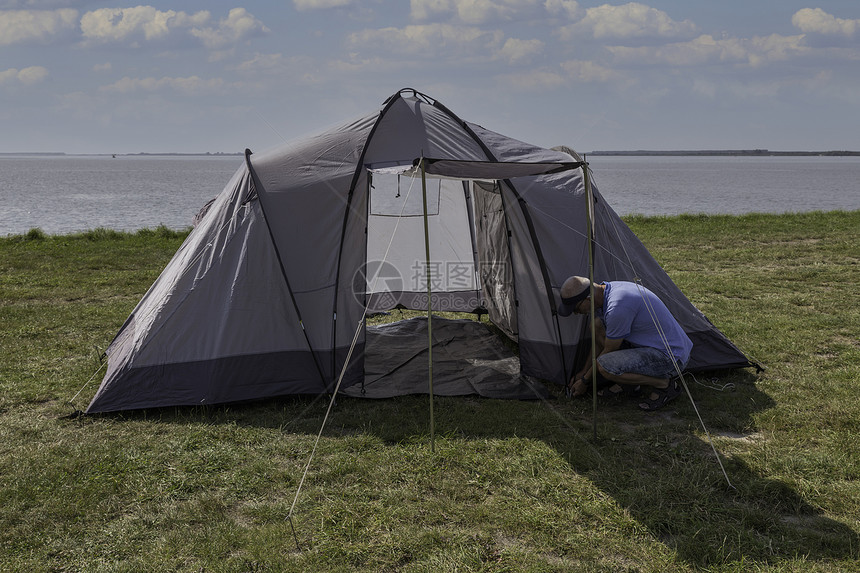 哈林弗利特绿色户外成年男子在靠近水的田地上搭起帐篷和挂钉子在湖边附近一个美丽的空间上架起帐篷在水线上架起帐篷图片