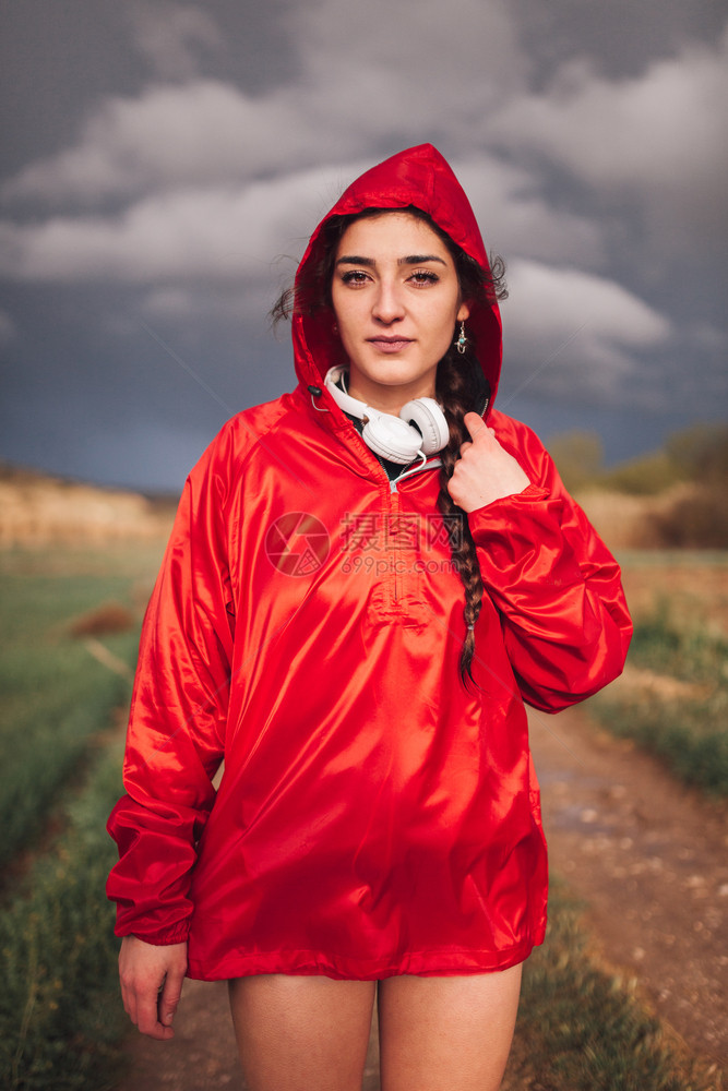 放松鸡皮疙瘩夏天年轻女子在雨与衣和耳机一起站在田地上图片