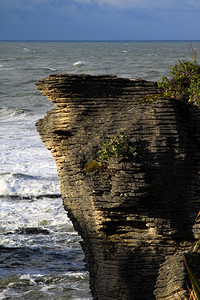 沉淀岩石在海浪背景下温暖的阳光单煎饼岩在海水和浪的背景下塔图片