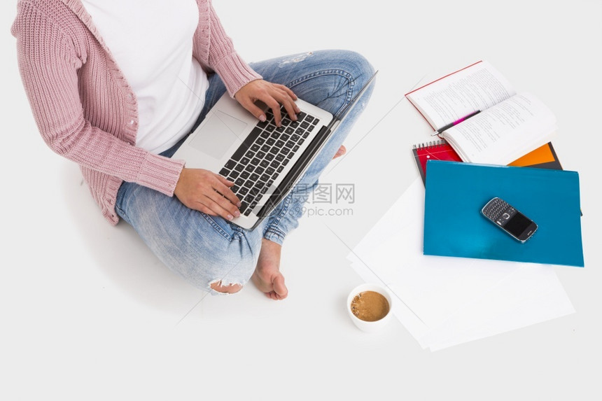 越过随意的年轻女学生用笔记本电脑工作双腿跨大坐在白背景上孤立的年轻女学生技术图片