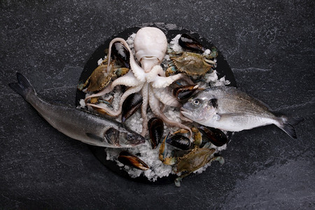 生的贝壳蛤蜊冰海白鱼蓝螃蟹和大理石桌上的多拉图片