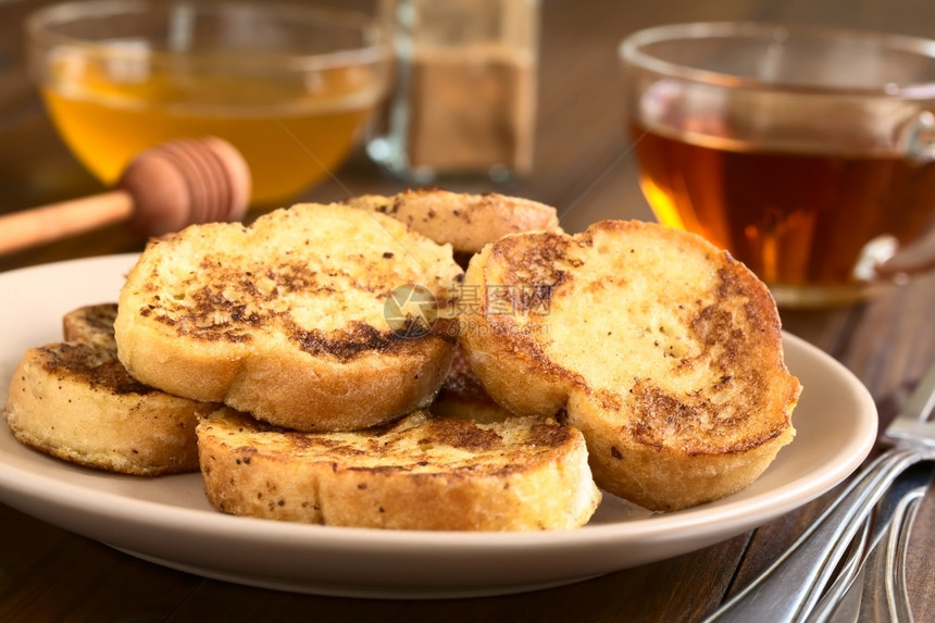 油炸法式吐司由面包蜂蜜肉桂粉和茶杯制成背面用天然光拍攝有选择焦点关注上层烤面包的前边缘甜点托里亚图片