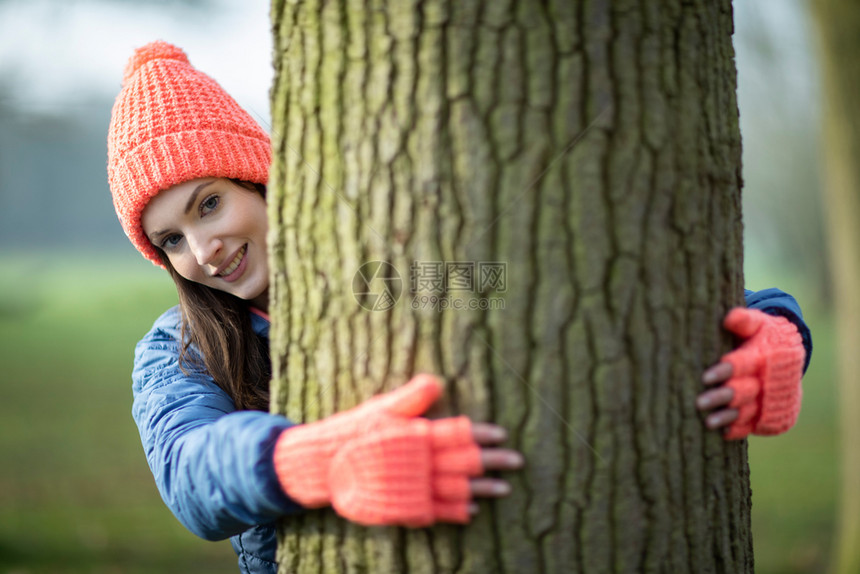 妇女穿戴手套的肖像在乡村边上冬季漫步时缠着树干人们正念森林图片
