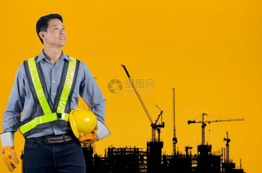 建设者亚洲工程师在新高楼公寓大和建筑起重机的背景上为工人安全持有黄色头盔而在昏日落时持色头盔的亚洲工程师装载着黄色头盔的亚洲工程图片