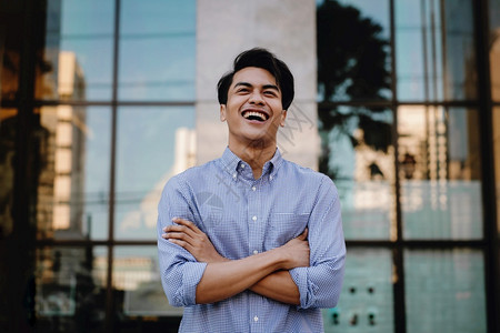 积极的随意笑亚裔青年商人在城市横跨双臂的肖像望着一个快乐的友善人模型图片
