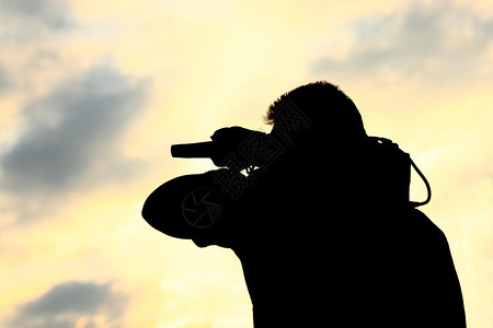 一个肩膀上带着电视摄像机的男人在日落时被锁住麦克风广播水平的图片