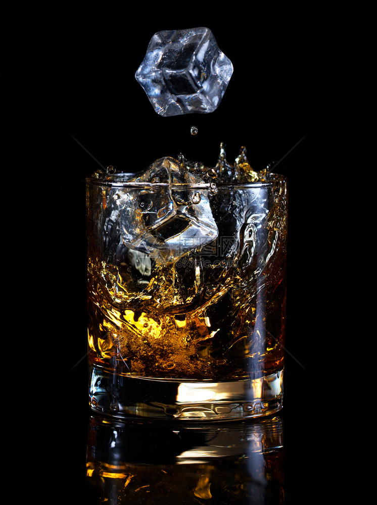 苏格兰人飞溅冰的立方体落在玻璃威士忌里孤立在黑色背景冰的立方体上倒在玻璃威士忌里图片