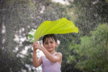 乐趣户外男孩微笑玩得开心站在她的头上叶子在雨中站立愉快图片