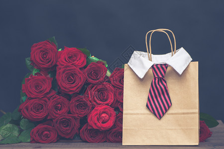 纸束给爱人一天礼物的概念一个男人的大红玫瑰和一个带棉皮领的礼物袋颜色图片