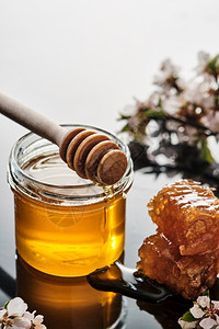一罐蜂蜜加窝和一棍在光背景上勺子美味的金图片