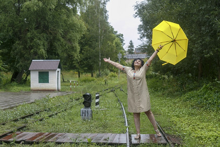 妇女站在铁路的轨上在雨季夏日扶着黄色雨伞追踪独自的火车图片
