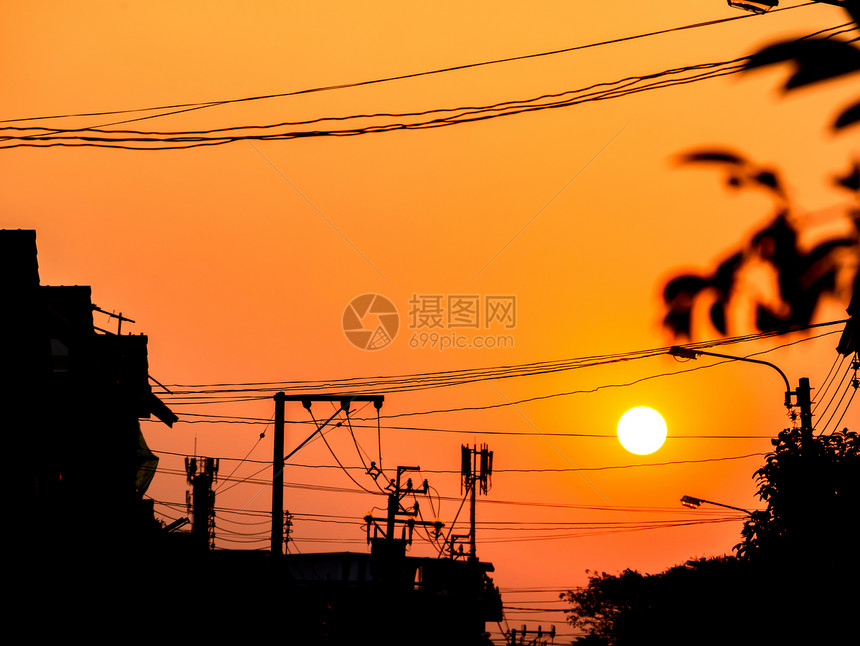 自然橙色天空在太阳周光电线杆树和建筑物后面日落泰国轮廓极图片