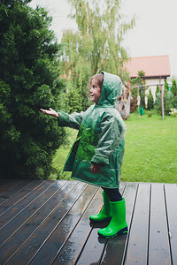穿着雨衣的女孩常设天气检查快乐笑的小女孩站在门廊上抓住雨滴穿着绿色衣背景