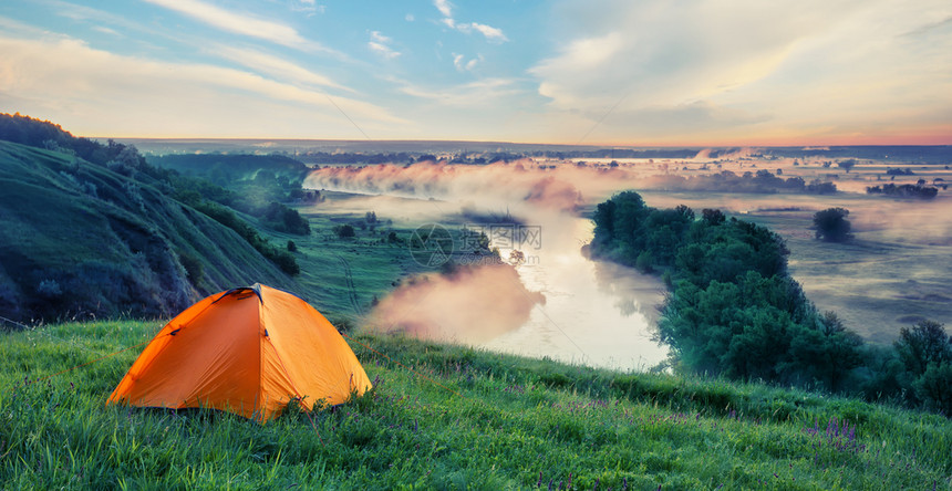 自然山上的橙色旅游帐篷在小河的夏季风景上方有绿草孤独自由的概念和在小里夫上方带绿草的山橘色旅游帐篷行绿色夏天图片