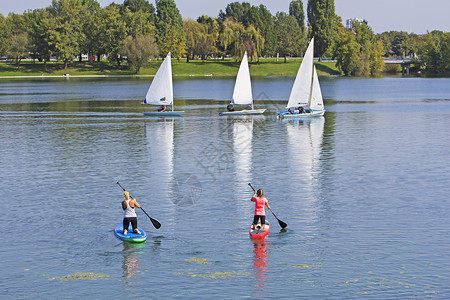 放松积极的娱乐两名妇女坐在桨板上三艘船在湖里航行图片