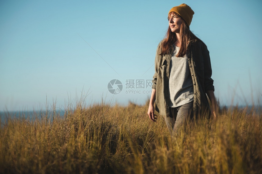 自然海美丽的女人有黄色帽子在高草地上行走徒步旅者图片