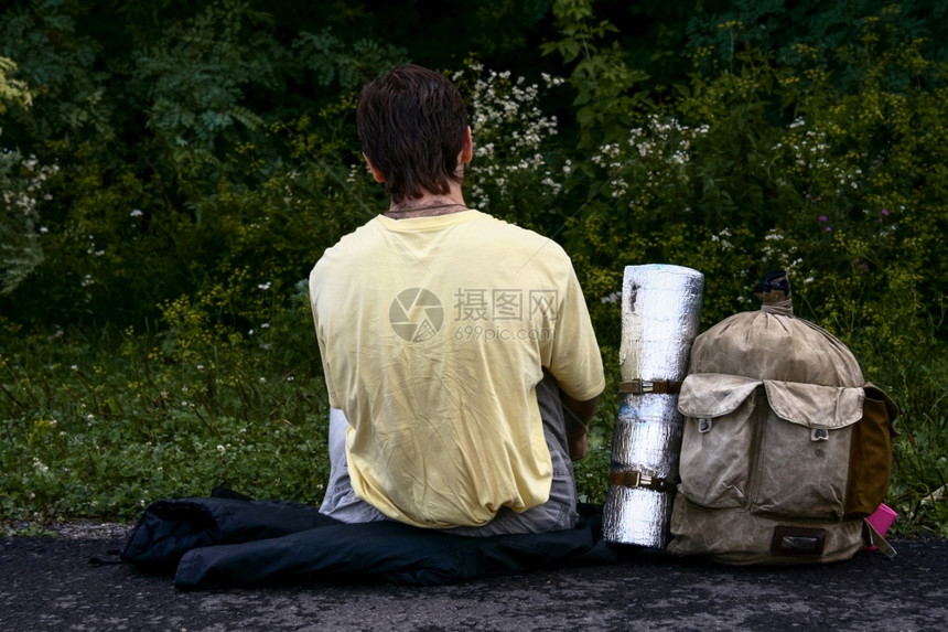旅行冒险后部背着面看远足者包坐在森林旁边的公路上图片