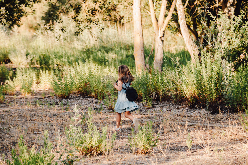 金发年轻女孩在田里跑身着洋装手握放大玻璃杯背包乐趣女微笑图片