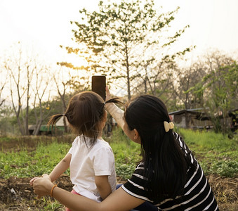 公园自然一种亚洲小女孩在日落背景下和母亲一起在花园里拍照的背影但图片