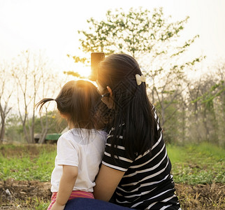 绿色服用亚洲小女孩在日落背景下和母亲一起在花园里拍照的背影但父母图片