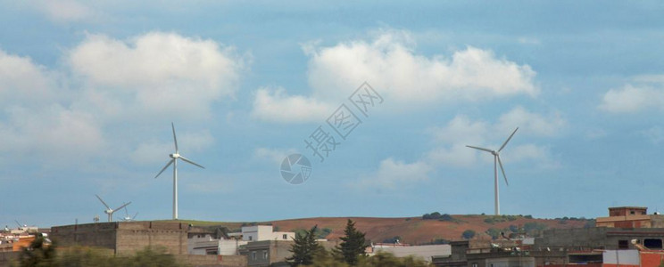 农场生产风车突尼斯沙漠中的风能强涡轮机站和城市风景与蓝色云天空的对比图片