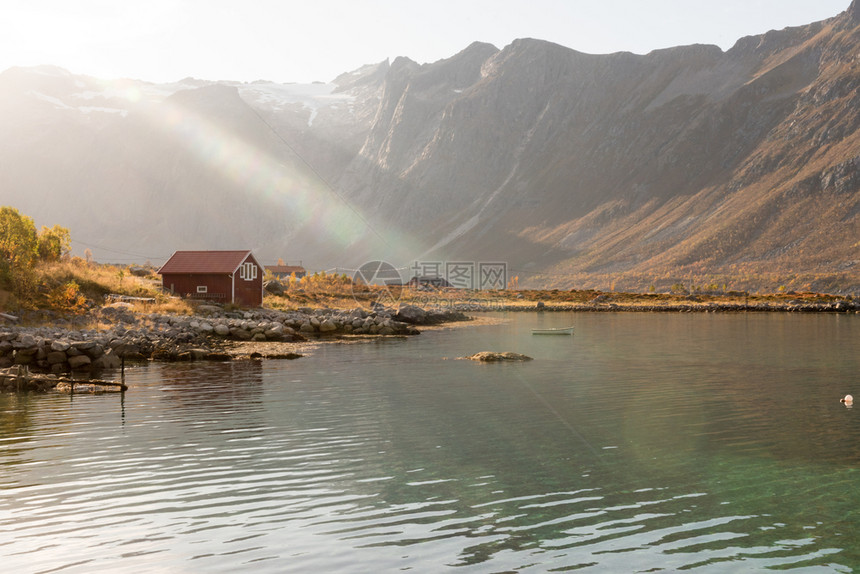 水美丽反射在挪威特罗姆索海岸的一座小屋上山峰顶在景色优美的农村风景中闪耀着光亮的束和透照明图片
