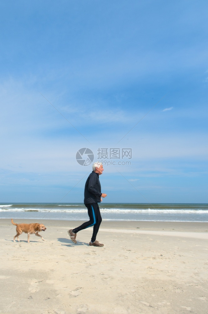 积极的成人健康老与狗一起在冬季沙滩上奔跑男人图片