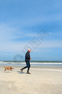 积极的成人健康老与狗一起在冬季沙滩上奔跑男人图片