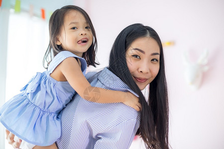 女肖像微笑快乐的亚洲小女孩在她母亲的背上在房子里图片