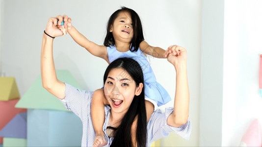 可爱的俏皮快乐亚洲小女孩在她母亲的背上在房子里童年图片
