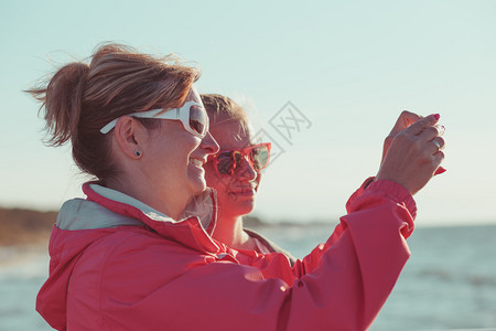 太阳镜海洋暑假期间母亲和女儿在海上用智能手机照相拍摄片的背面景象晴天图片