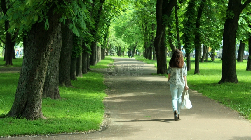 年轻女子在美丽的公园上行走有很多绿树女游览人行道图片