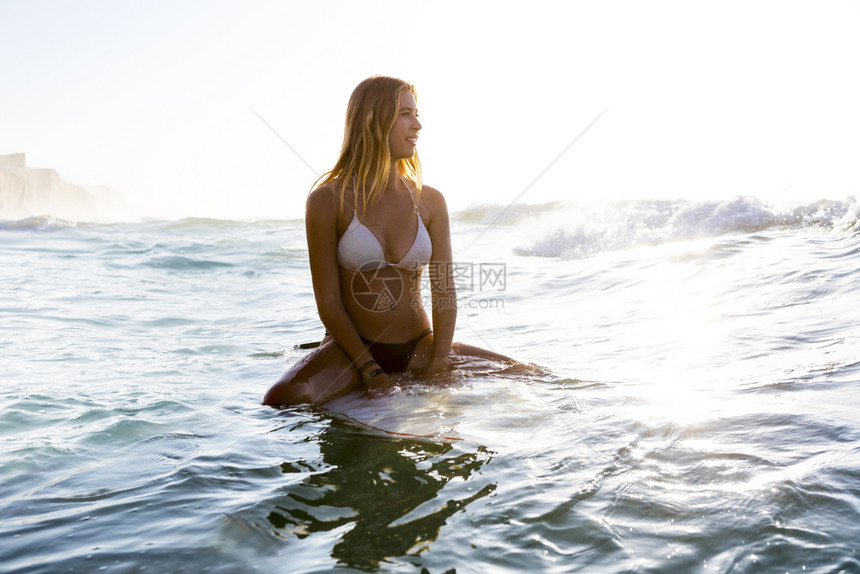 坐在冲浪板上等待海浪的美丽年轻女士图片