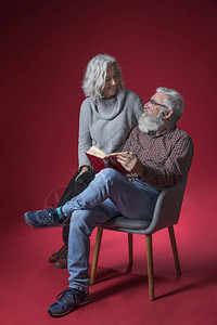 与丈夫坐在椅子上的丈夫坐在一起高级妇女在红色背景下握着书手织物动花朵图片